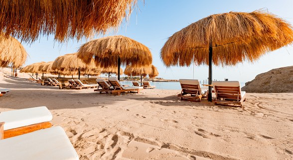 Sandstrand mit Sonnenliegen und Sonnenschirmen aus Stroh