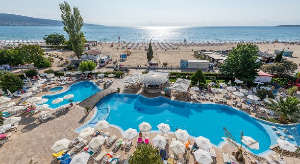 Hotel Sentido Neptun Beach Poollandschaft: großer Pool, Liegestühle, Sonnenschirme, umgeben von Palmen und Meerblick, klarer Himmel.