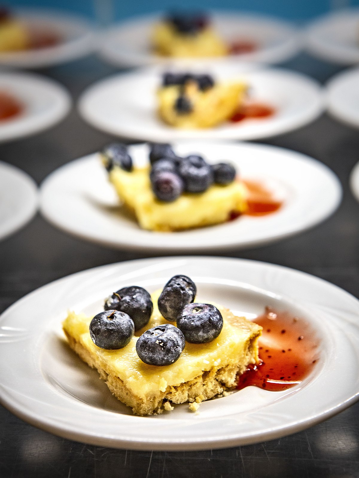 Hotel Sentido Orosei Beach, Sardinien, Nahaufnahme eines Desserttellers mit Käsekuchenstück, frischen Blaubeeren und roter Fruchtsauce – appetitlich angerichtet.