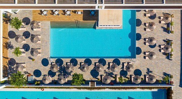 **Alt-Text (max. 120 Zeichen):** Luftaufnahme eines rechteckigen Pools mit Liegen, Sonnenschirmen und angrenzendem Wasserkanal in moderner Hotelanlage.