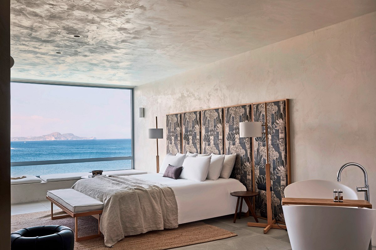 Stilvolles Schlafzimmer mit frei stehender Badewanne, großem Fenster und Blick auf das Meer und tropische Vegetation.
