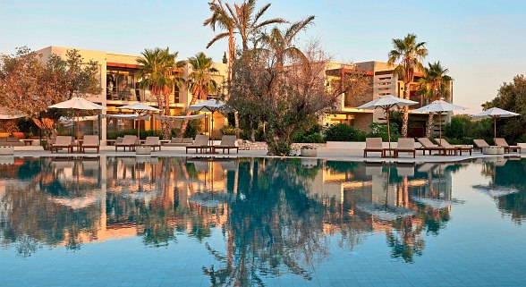 Moderner Resortpool mit eleganten Liegen und Palmen, ideal zum Entspannen unter der mediterranen Sonne.