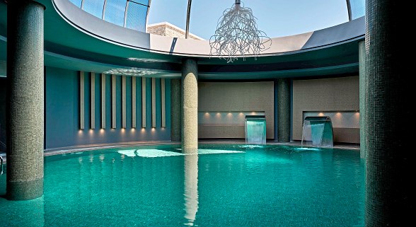 Eleganter Innenpool mit Wasserfällen und Tageslichtkuppel – perfekte Entspannung in stilvoller Spa-Atmosphäre.