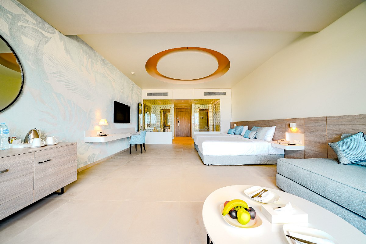 Modernes Hotelzimmer mit zwei Einzelbetten, gemütlichem Sofa und großem Fenster zum Garten oder Balkon.