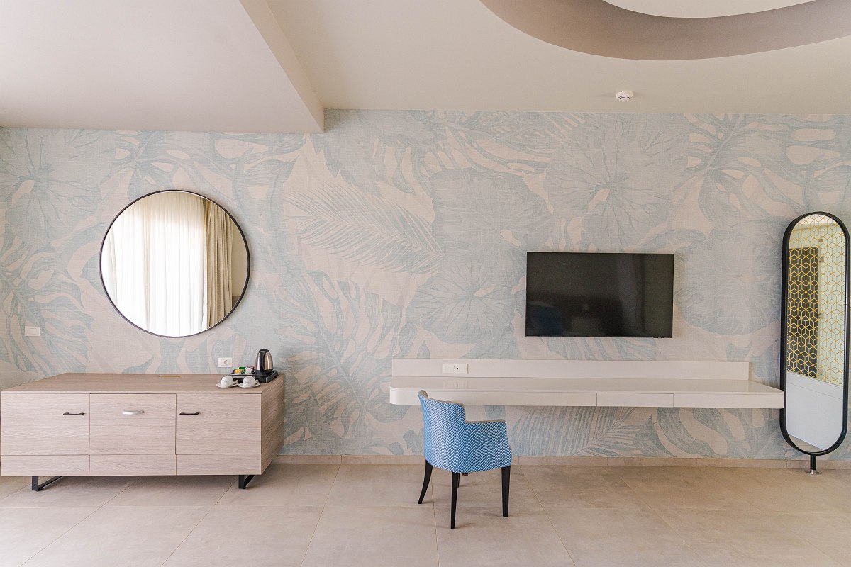 Modernes Hotelzimmer mit großem Spiegel, zwei Einzelbetten, TV und Balkon mit Meerblick.