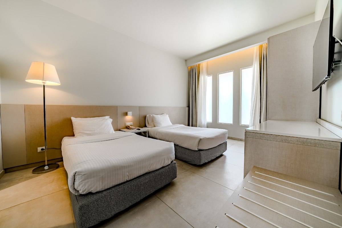 Modernes Hotelzimmer mit Doppelbett, Schreibtisch, maritimer Wandkunst und Balkon mit Meerblick und Palmen im Hintergrund.