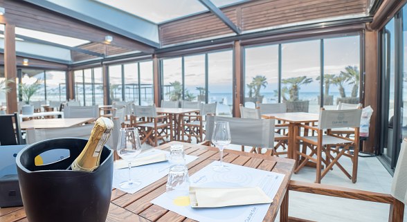 Elegantes Restaurant mit Holztischen, Stühlen, gedecktem Tisch mit Sekt und Blick auf das Meer.