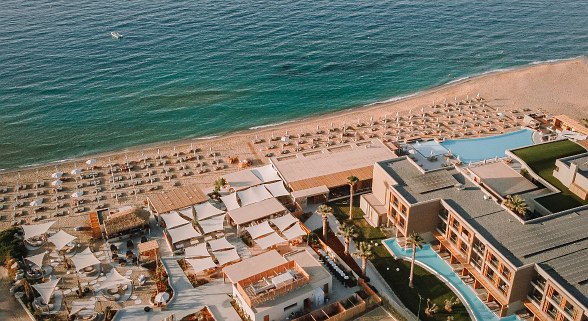 Luftaufnahme eines modernen Strandresorts mit Poollandschaft, Sonnenschirmen und direktem Zugang zum Meer.