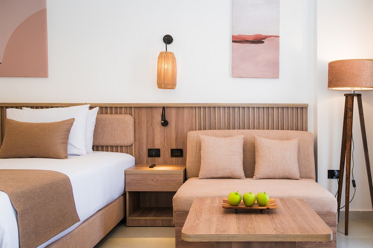 Großzügiges Hotelzimmer mit gewölbter Decke, Doppelbett mit roten Akzenten, Sitzbereich und Balkon mit Ausblick auf die Stadt.