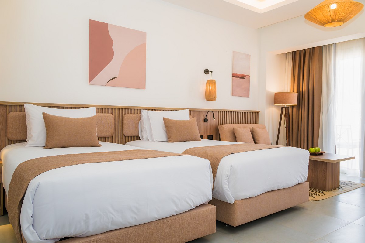 Helles Hotelzimmer mit gewölbter Decke, zwei Einzelbetten, blauen Akzenten, Obstteller, Flachbild-TV und modernem Interieur.