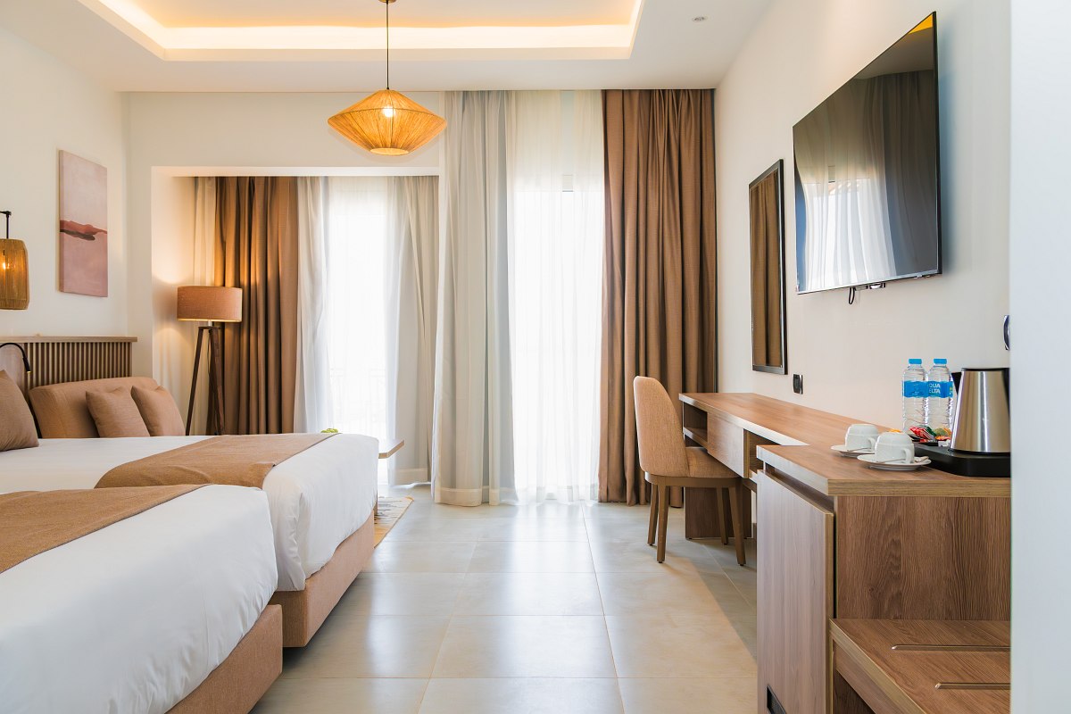 Elegantes Hotelzimmer mit Doppelbett, blauen Akzenten, gewölbter Ziegeldecke, Balkon und Blick auf die Poolanlage.