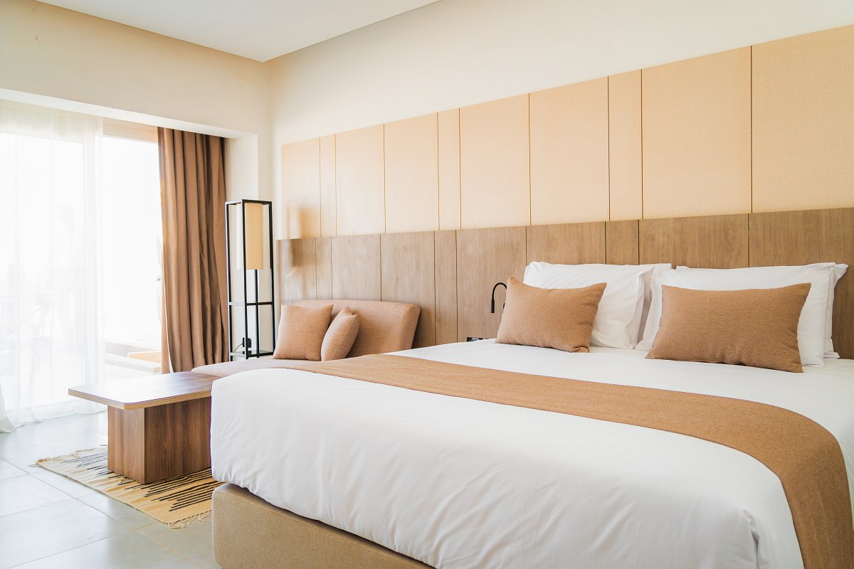 Modernes Hotelzimmer mit Doppelbett, blauen Akzenten, gewölbter Ziegeldecke und Balkon mit Blick auf die Hotelanlage.