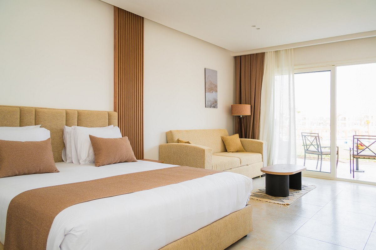 Stilvolles Hotelzimmer mit Doppelbett, blauen Akzenten, gewölbter Backsteindecke und Balkon mit Blick auf eine Resortanlage.