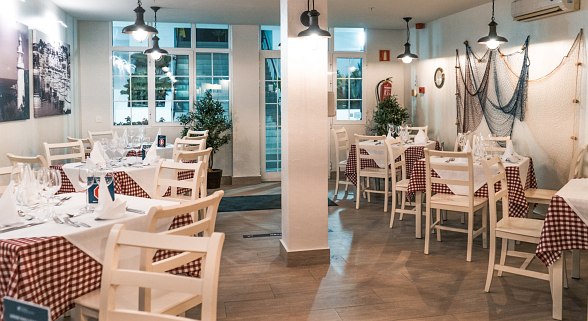 Cozy restaurant with maritime decoration, checkered tablecloths, white furniture and laid tables.