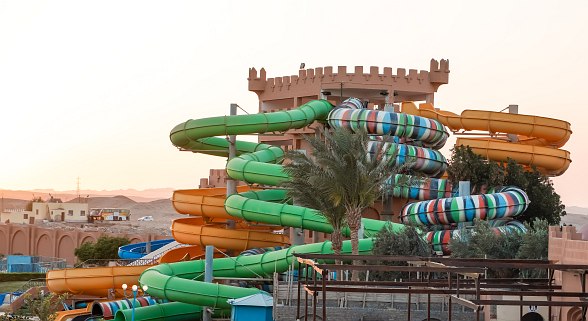 Water park with colorful slides in front of a castle-like building, several slides lead into a large swimming pool.