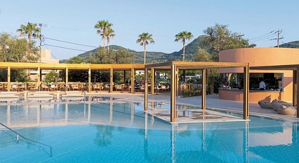 Outdoor water park with colorful slides, a pool, surrounded by trees and flowers. Comfortable lounge chairs and umbrellas provide relaxation spots.