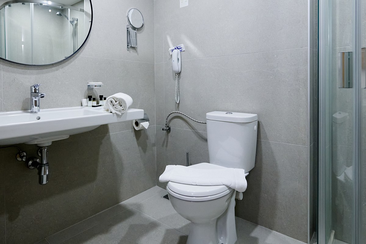Modern bathroom with toilet, washbasin, mirror, hairdryer and shower cubicle, light gray tiles.
