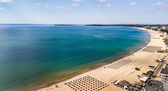  Hotel Sentido Bellevue Beach at the beach with many sunbeds and hotels in the background under a blue sky.