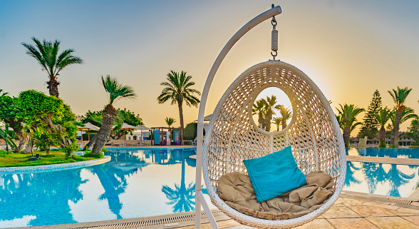 Woman in sun lounger by the pool with palm trees at sunset in a tropical hotel resort.