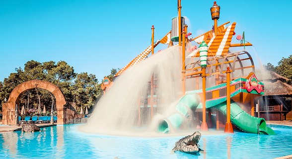 Large water feature with pirate ship and slides, which is currently pouring a huge waterfall into a children's pool.