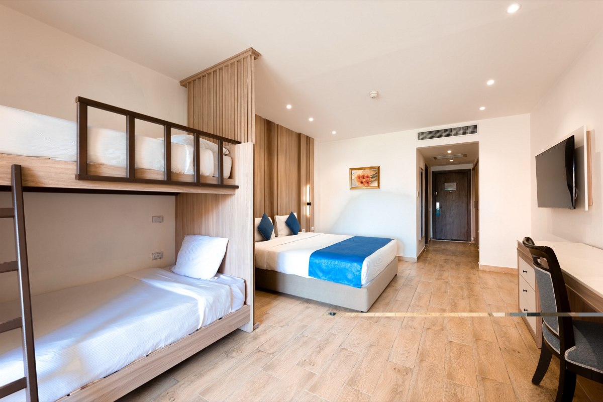 Spacious room with wood floors, double bed with blue bedding, bunk beds, desk, TV, and modern lighting. Simple and bright design.