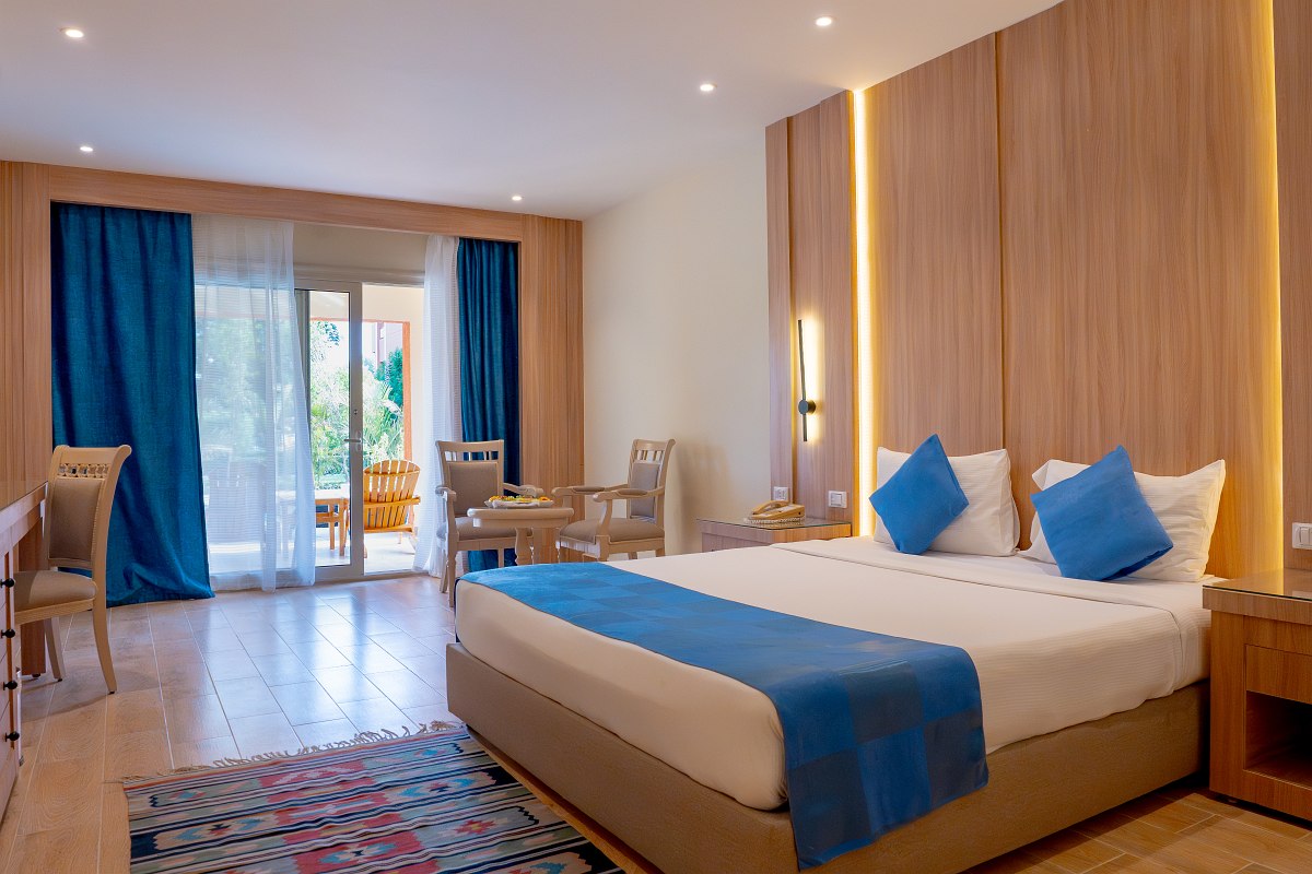 Modern room with wood floors, double bed with blue bedding, bunk beds, wall-mounted TV, and pink accent wall featuring a white palm tree design. Bright and cozy.