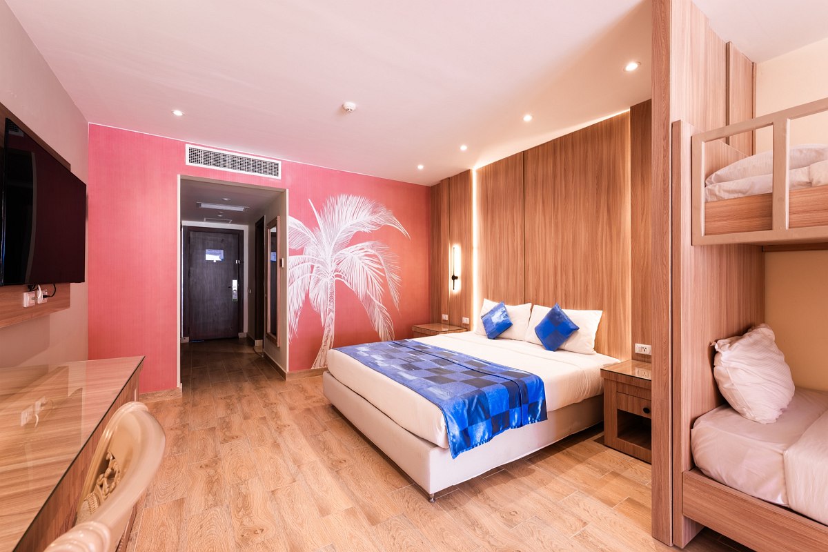 Modern room with wood floors, double bed with blue bedding, bunk beds, wall-mounted TV, and pink accent wall featuring a white palm tree design. Bright and cozy.