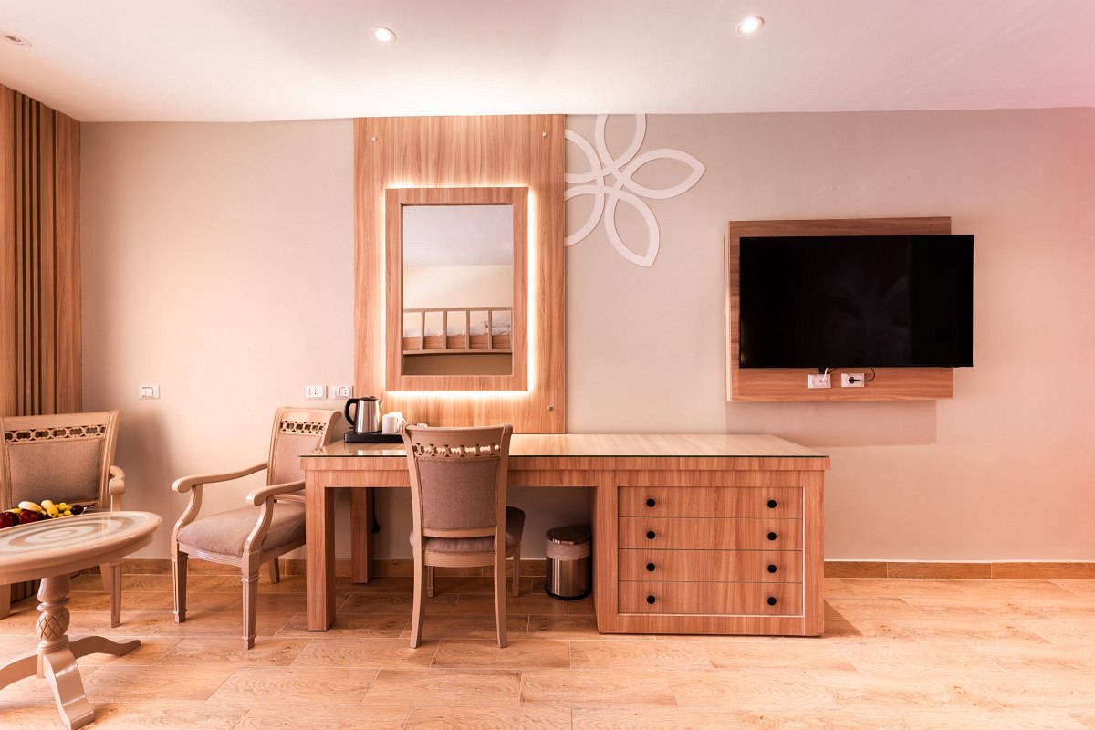 Modern hotel room with desk, TV, two chairs, small table, large mirror, and warm-toned marble floor. Cozy and elegant design.