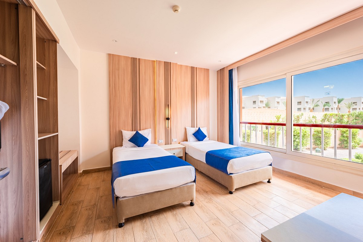 Bright room with two single beds, wooden floors, and large windows offering a garden view. Clean and minimalistic.