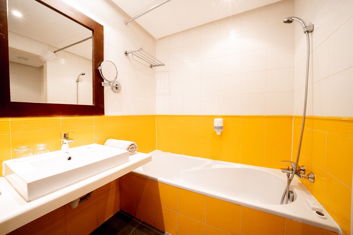 Modern bathroom with yellow tiles, bathtub and shower, bright and clean.
