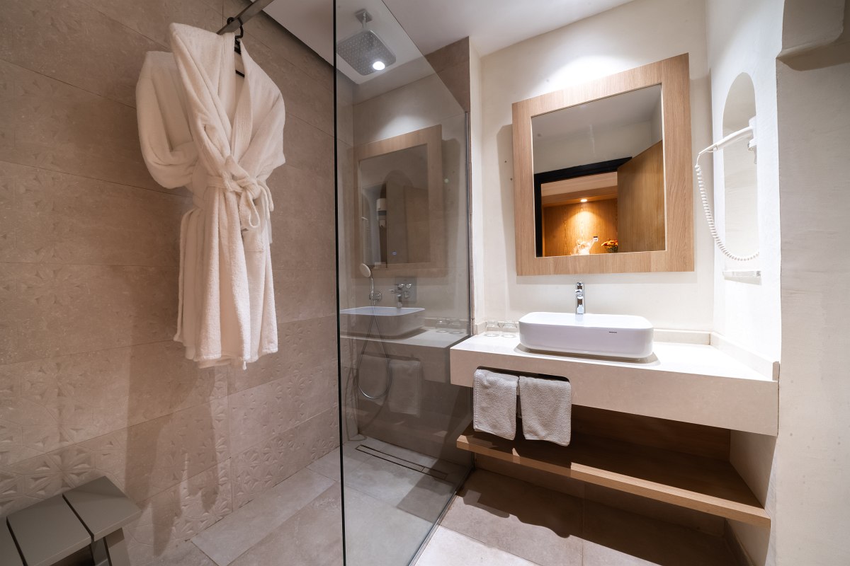 Modern hotel bathroom with large shower, washbasin, mirror, bathrobe and towels.