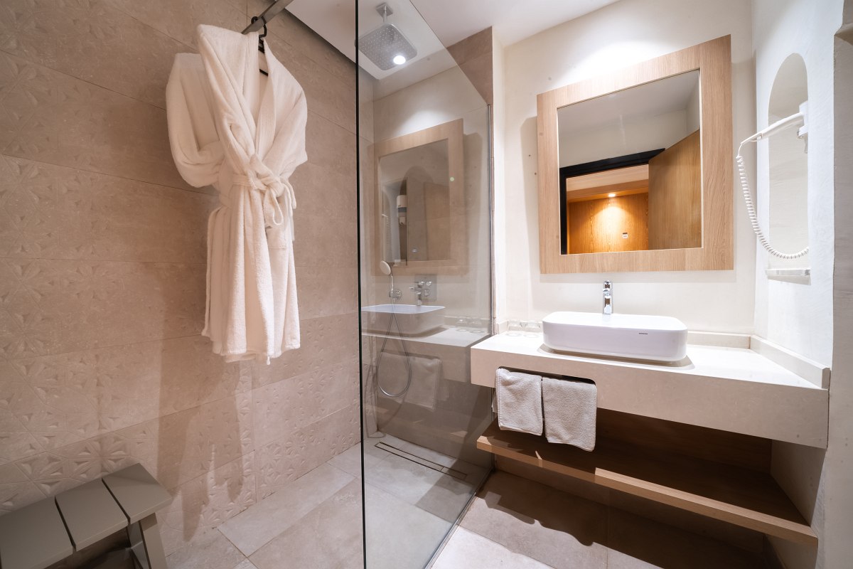Modern hotel bathroom with large shower, washbasin, mirror, bathrobe and towels.
