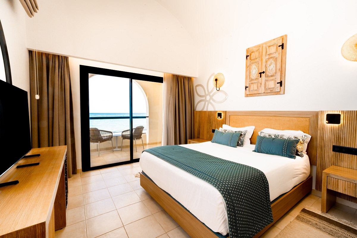 Bright hotel room with double bed, desk, oriental carpet and minimalist furnishings.