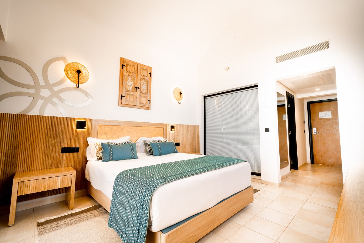 Bright hotel room with double bed, desk, oriental carpet and minimalist furnishings.