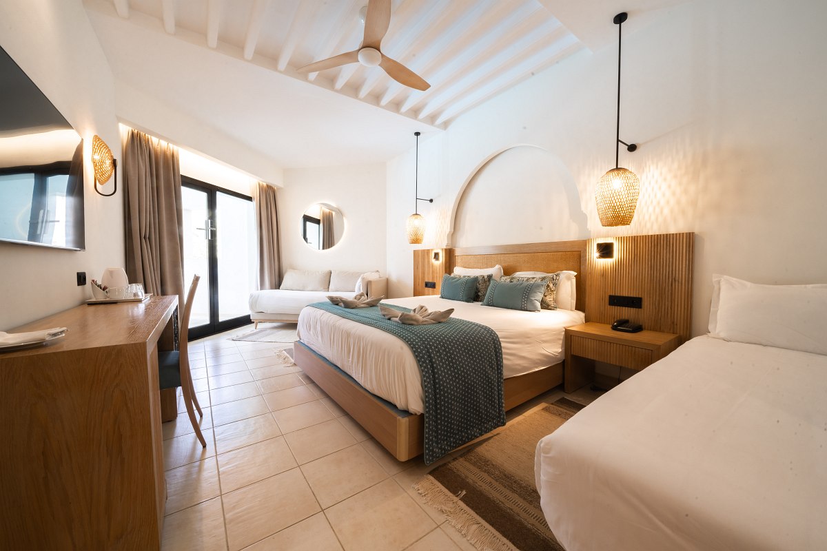 Bright hotel room with double bed, single bed, sofa, desk and stylish lighting.