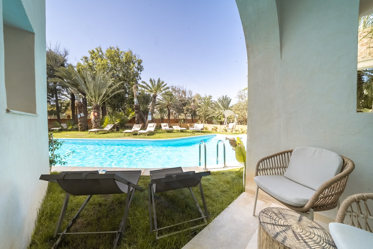 Terrace with seating furniture and direct access to the pool, surrounded by palm trees and sun loungers.