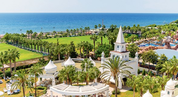 Hotel complex with palm trees, extensive gardens, white towers and views of the deep blue Mediterranean.