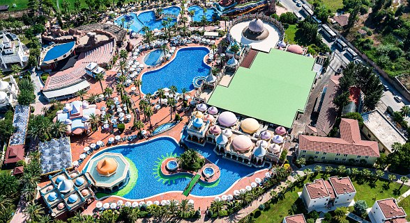 Aerial view of an extensive hotel complex with pools, slides, sunshades and oriental architecture.
