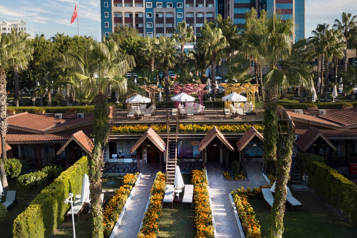 View of a well-kept hotel complex with small garden bungalows, flowering paths and a modern main building in the background.