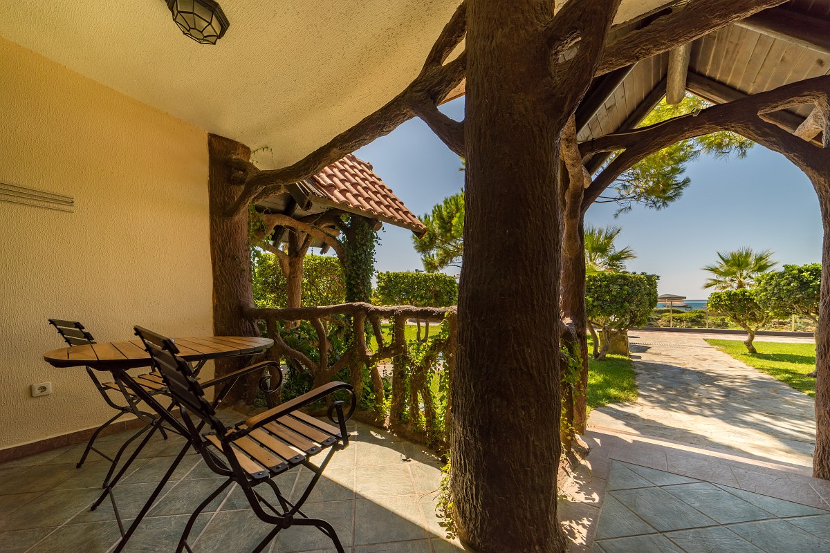 Covered terrace with rustic wooden elements, seating area and view of the garden and sea in the background.