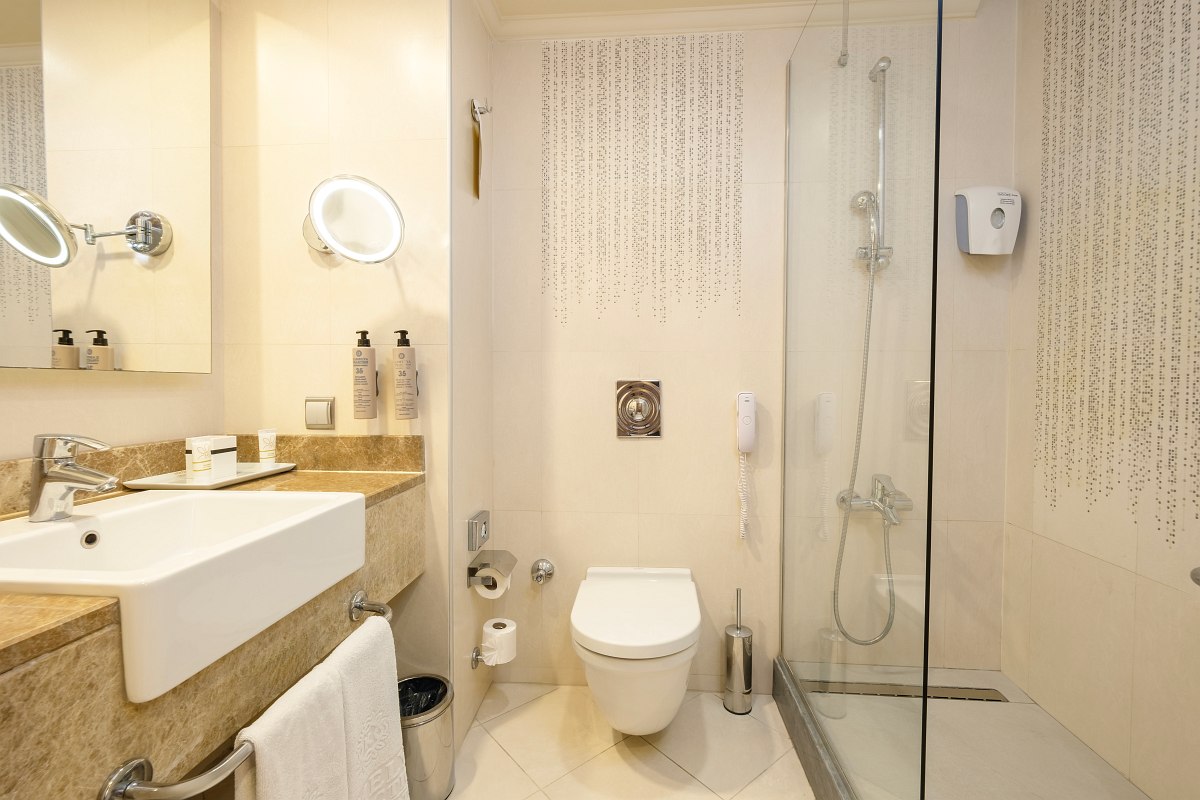 Modern hotel bathroom with large shower, WC, washbasin, mirror and stylish wall decorations in neutral tones.