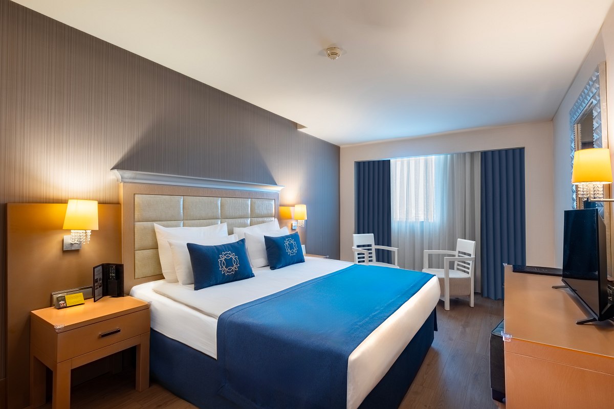 Bright double room with king-size bed, elegant design in blue and beige and seating area in front of the window.