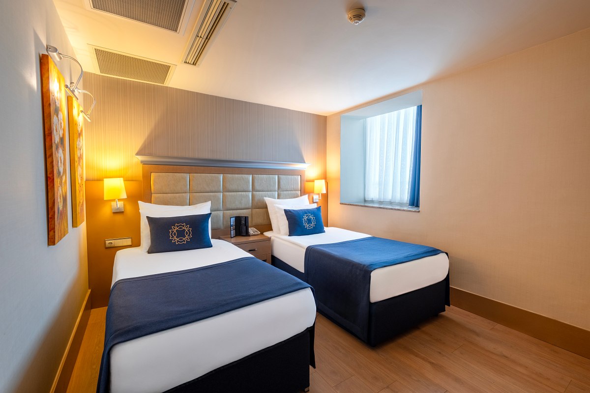 Modern room with two single beds, simple furnishings in blue-beige and daylight window.