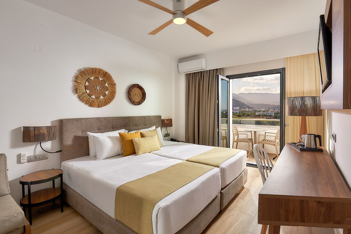 Bright bedroom with two beds, desk, TV, ceiling fan and balcony with a view.