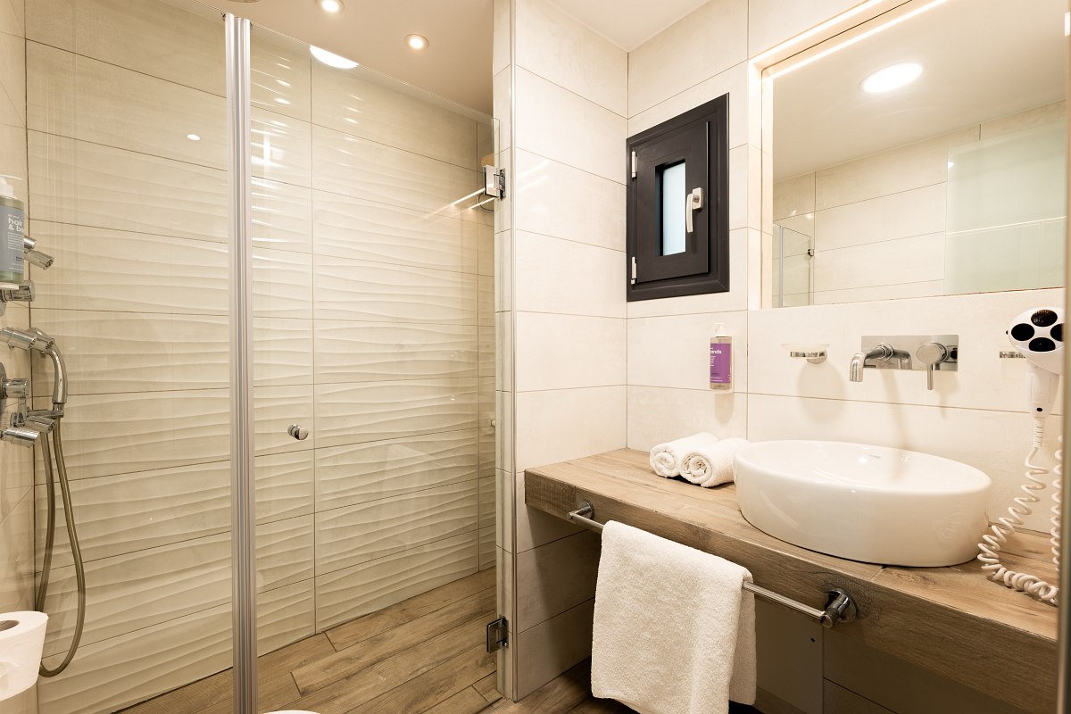 Modern, bright bathroom with glass shower, washbasin, round washbasin, illuminated mirror and towels.