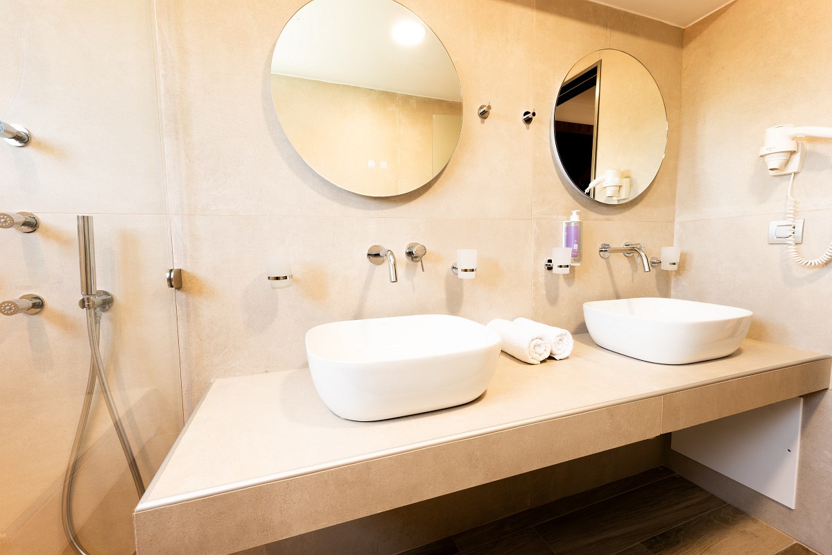 Modern hotel bathroom with two round mirrors, washbasin, towels and large walk-in shower.