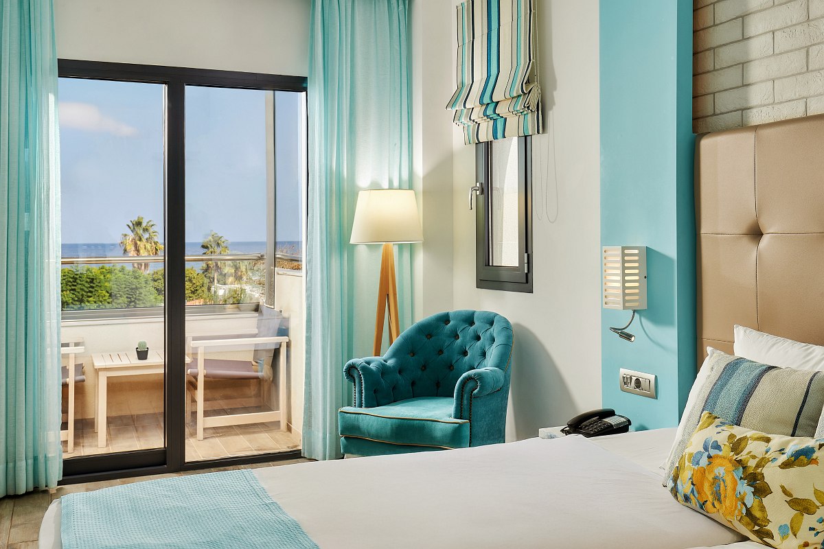 Modern, bright hotel room with double bed, sofa, wooden decor and balcony with a view of the mountains and nature.