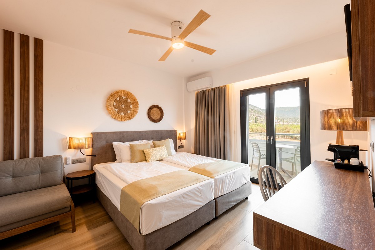 Modern, bright hotel room with double bed, sofa, wooden decor and balcony with a view of the mountains and nature.
