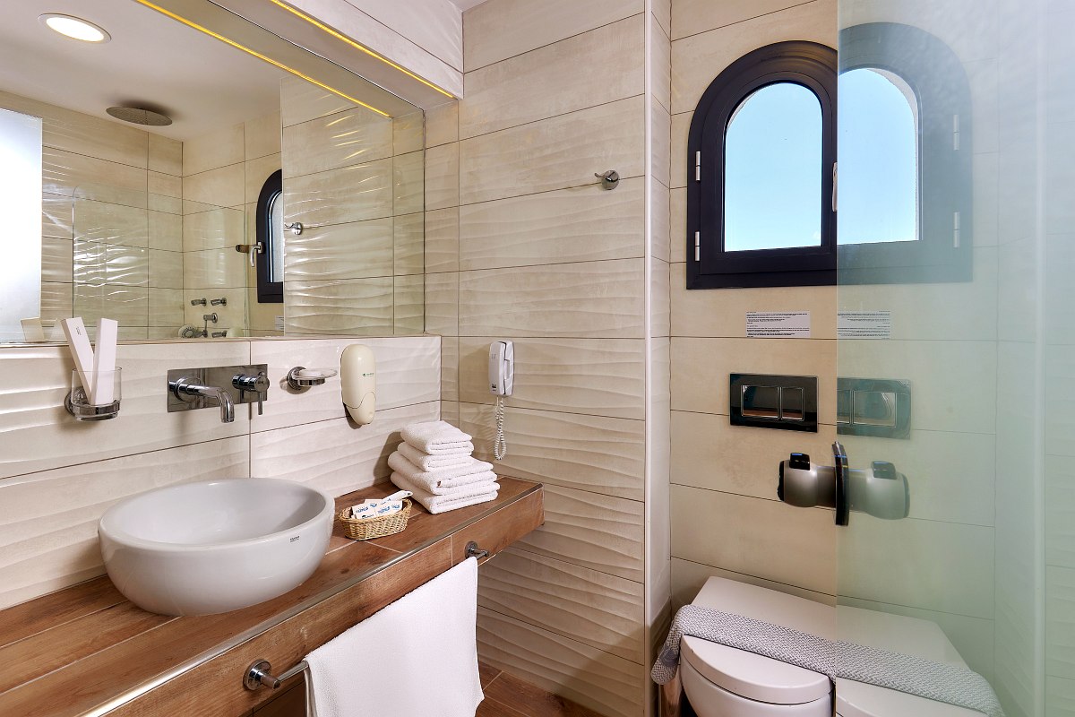 Bright hotel room with two single beds, armchair and balcony with sea view, modern, friendly furnishings in turquoise tones.