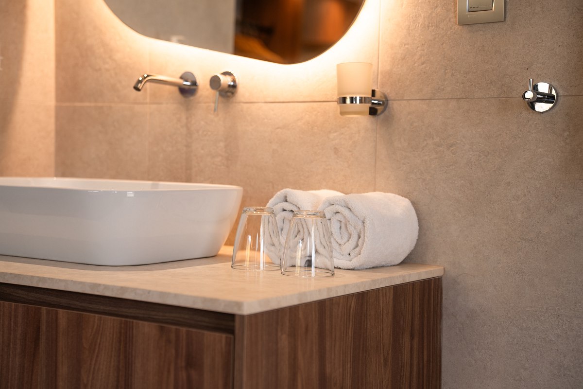 Close-up of a modern washstand with white towels, drinking glasses and stylish ceramic washbasin.